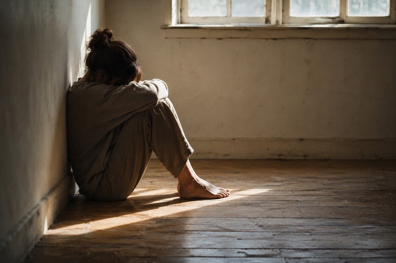 Person sitting quietly against a wall in a sunlit room, conveying groundedness, grief, and resilience.